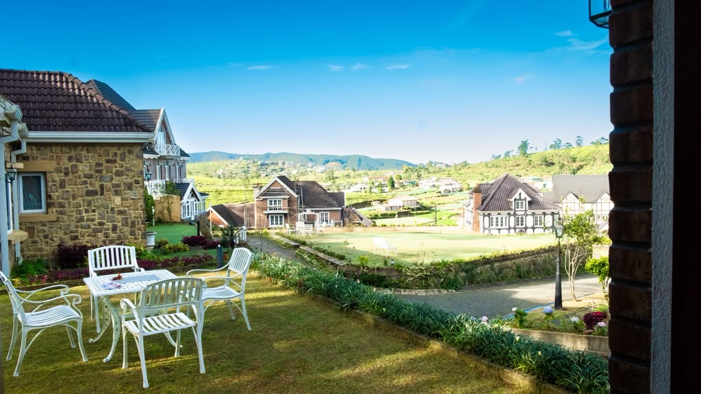 Garden chairs on a lawn at Little England, looking over the cottages to the hills
