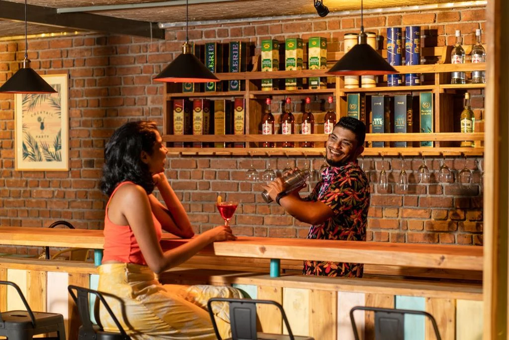 A bartender mixing a cocktail for a guest at the brick-walled bar