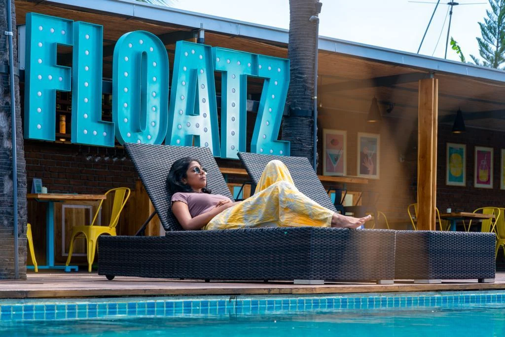 A guest relaxing on a poolside lounger beneath the Floatz sign