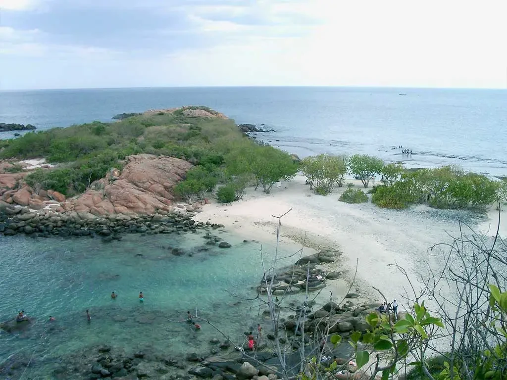 The rocky headland and white sand cove of Pigeon Island, with swimmers in the shallows