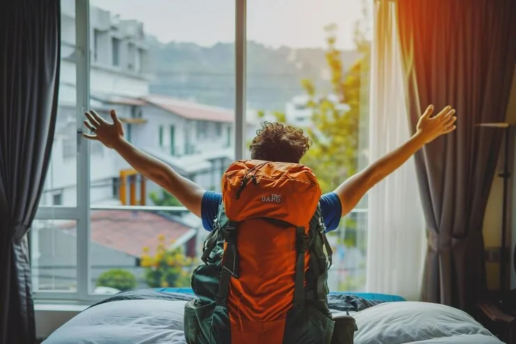 A traveller with a backpack stretching at a sunlit hotel window