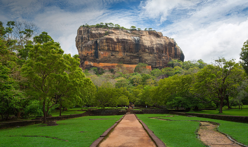 Sigiriya rock rising above the forest at the end of the garden path